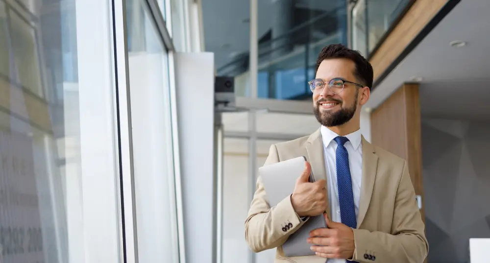 Smiling businessman with tablet by window.