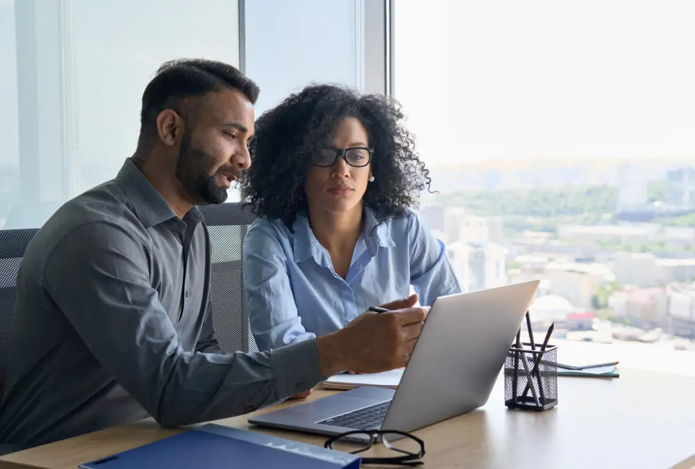 Two colleagues discussing work on laptop.